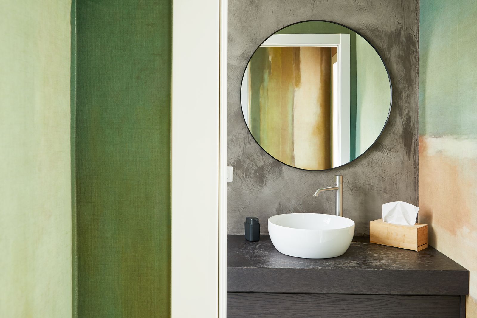 Elegant bathroom featuring green walls, a sleek sink, and a round mirror for a modern touch.