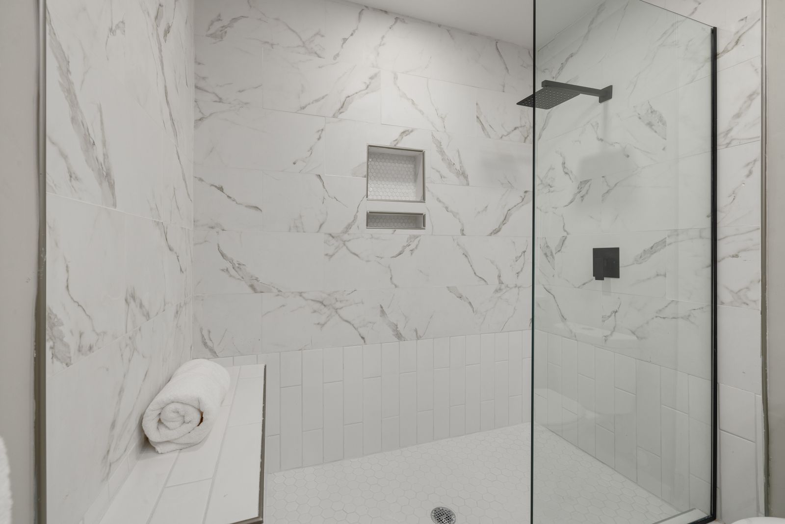 A bright walk-in shower with a glass panel, bench seat and grab bar